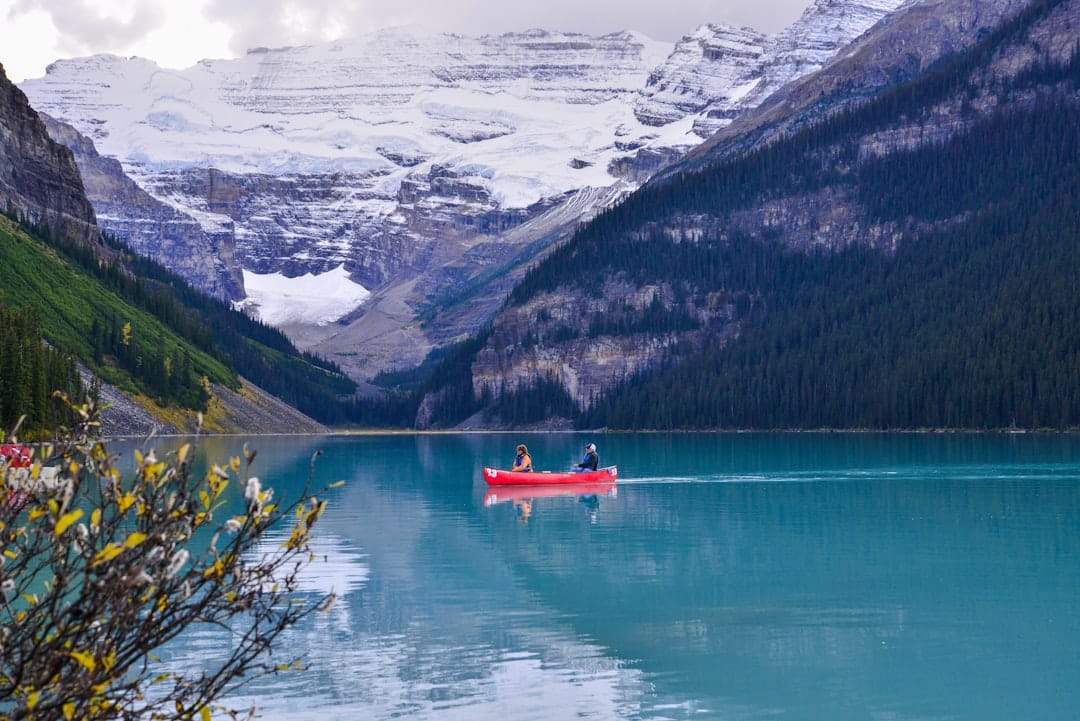 Two people paddling a red canoe on turquoise Lake Louise with Rocky Mountains in the background