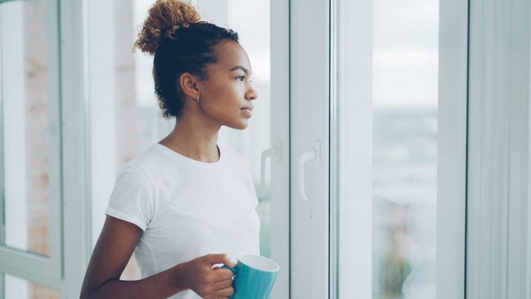 Woman holding a warm mug looking out a window enjoying a calm morning routine