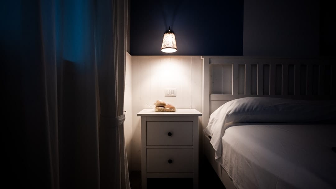 Warm bedside lamp illuminating a nightstand next to a bed, creating a peaceful sleep environment