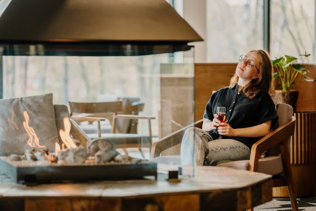 Woman relaxing by a modern fireplace with a warm drink in a cozy evening setting