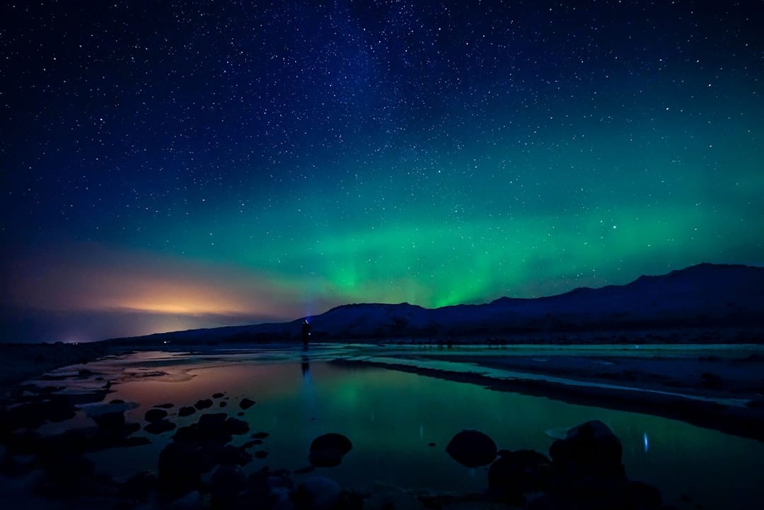 Northern lights aurora borealis glowing green and blue over mountains and a lake, representing cannabis delivery to Yellowknife Northwest Territories
